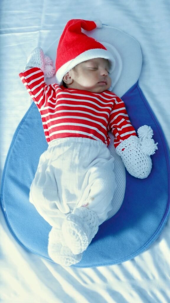 Cute newborn baby sleeping in a red Santa hat with striped shirt, perfect for holiday themes.