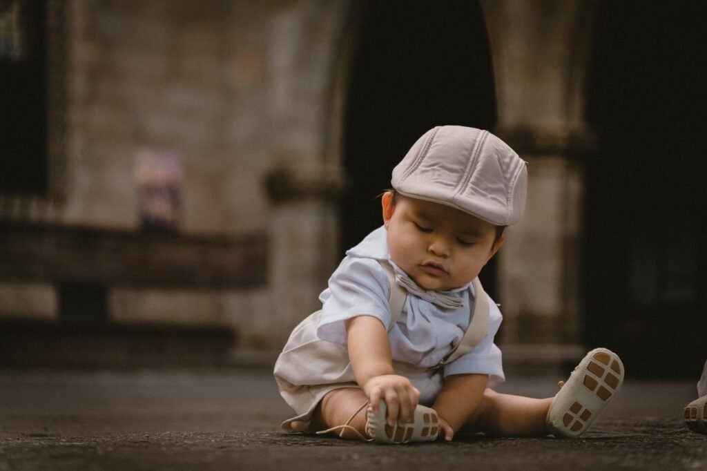 Charming baby boy sitting in an elegant courtyard, wearing a cap and shorts.