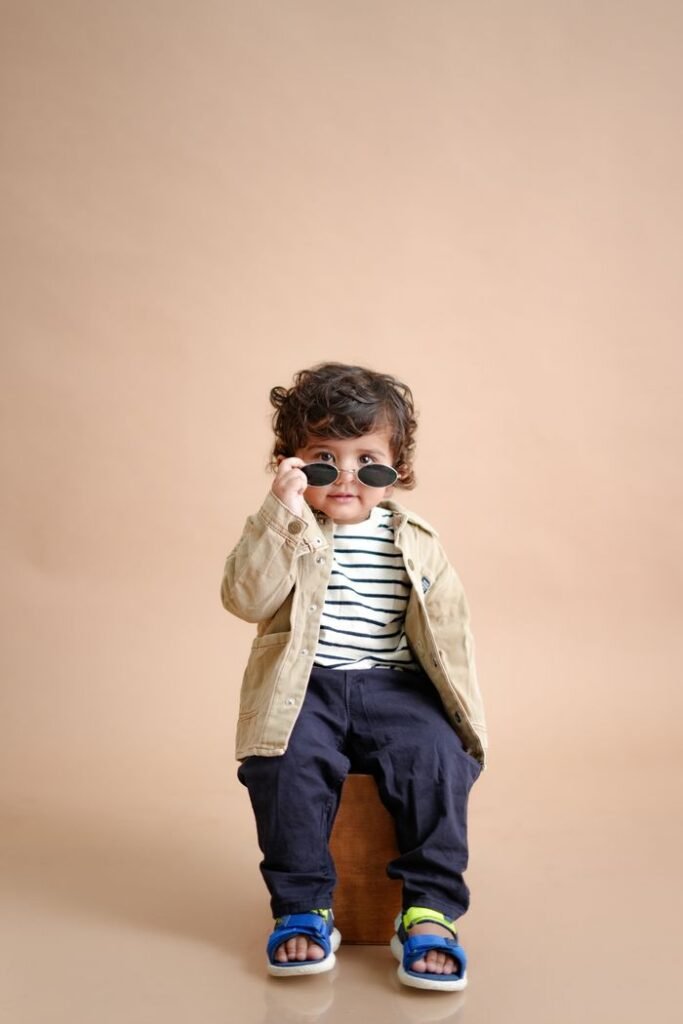 Charming toddler wearing sunglasses and casual outfit on a neutral background, exuding style and confidence.