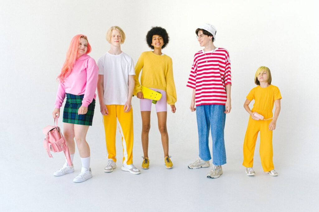 Full body group of positive multiethnic teenager friends with backpack and penny board standing against white wall and looking at camera