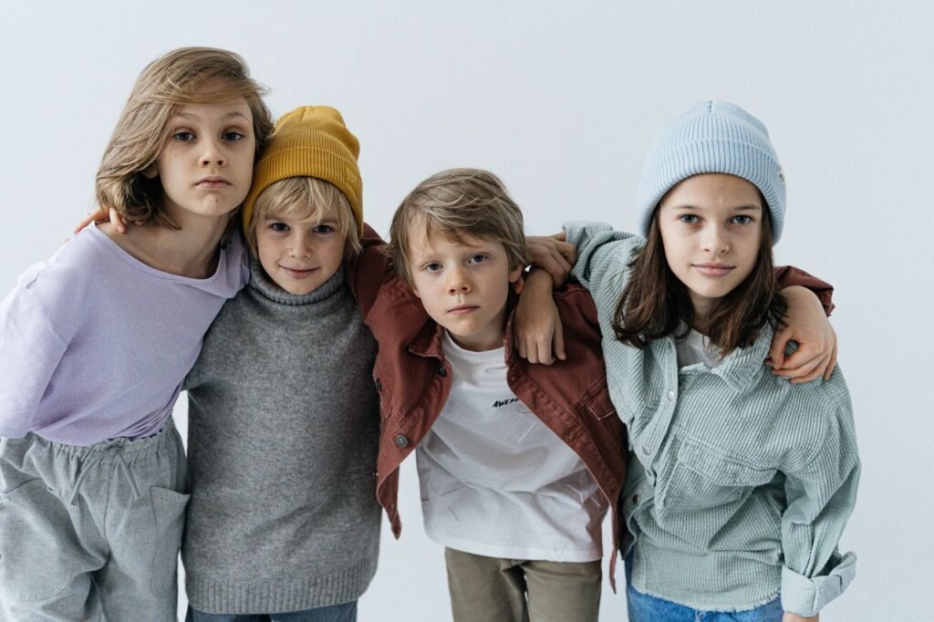 Children posing together in trendy casual outfits with hats indoors.