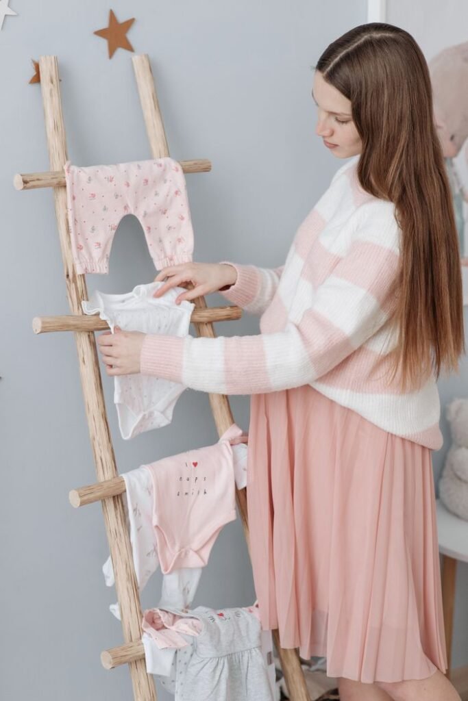 Pregnant woman arranging baby clothes on a wooden ladder in a cozy room.